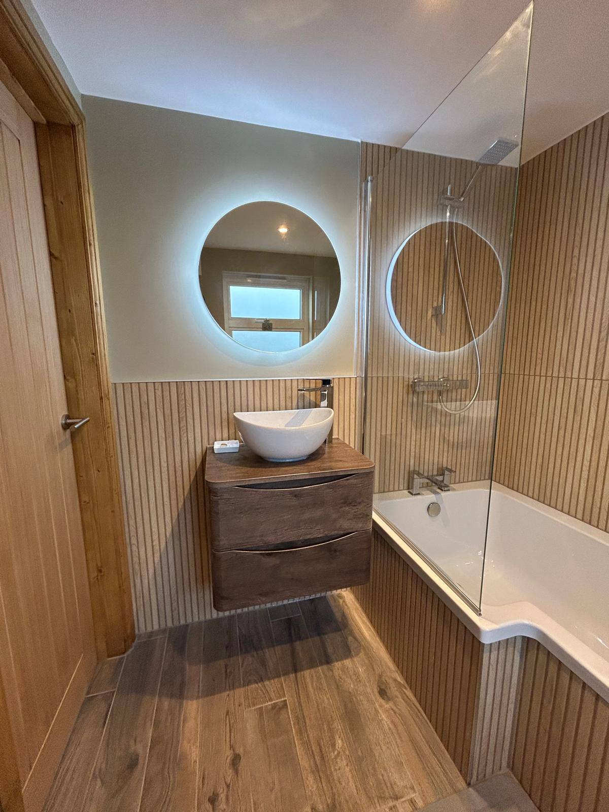 Wood slat bathroom with round LED mirror and bath